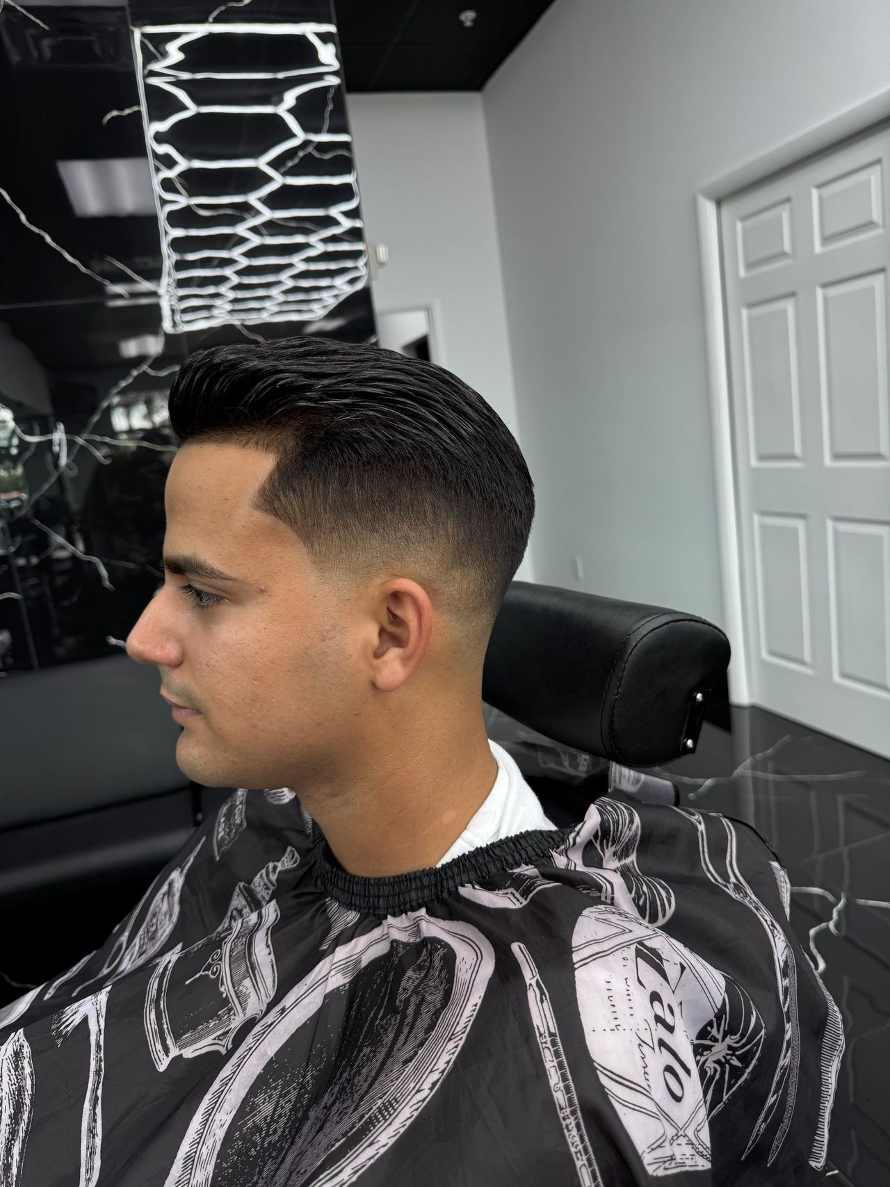 Slicked-back haircut with a low fade by Yoel Luxury Barber